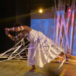 artista negra durante sua performance, presa numa teia branca