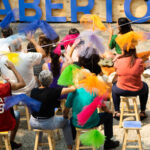 público de costas sentado em cadeiras brincam com fluflus coloridos
