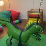 balanço em forma de inflável de um dinossauro verde suspenso e fixo no teto