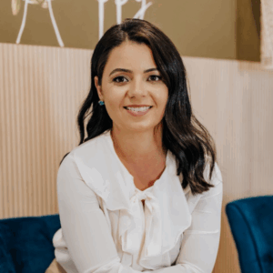 Aline Coelho é uma mulher branca, de cabelos pretos lisos e longos. Veste blusa branca.