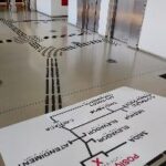em primeiro plano, mapa tátil do museu de congonhas. ao fundo, pisos táteis preto no piso bege claro