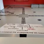 em primeiro plano, mapa tátil e, ao fundo, piso táteis pretos no piso branco do centro de referência ao barroco