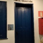 placa ao lado de porta azul de madeira na Administração FUMCULT