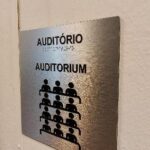 placa em chapa de metal com fontes pretas e braille do auditório da FUMCULT