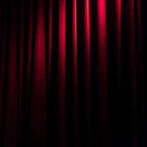 Cortina vermelha típica de teatro na penumbra com foco de luz no centro
